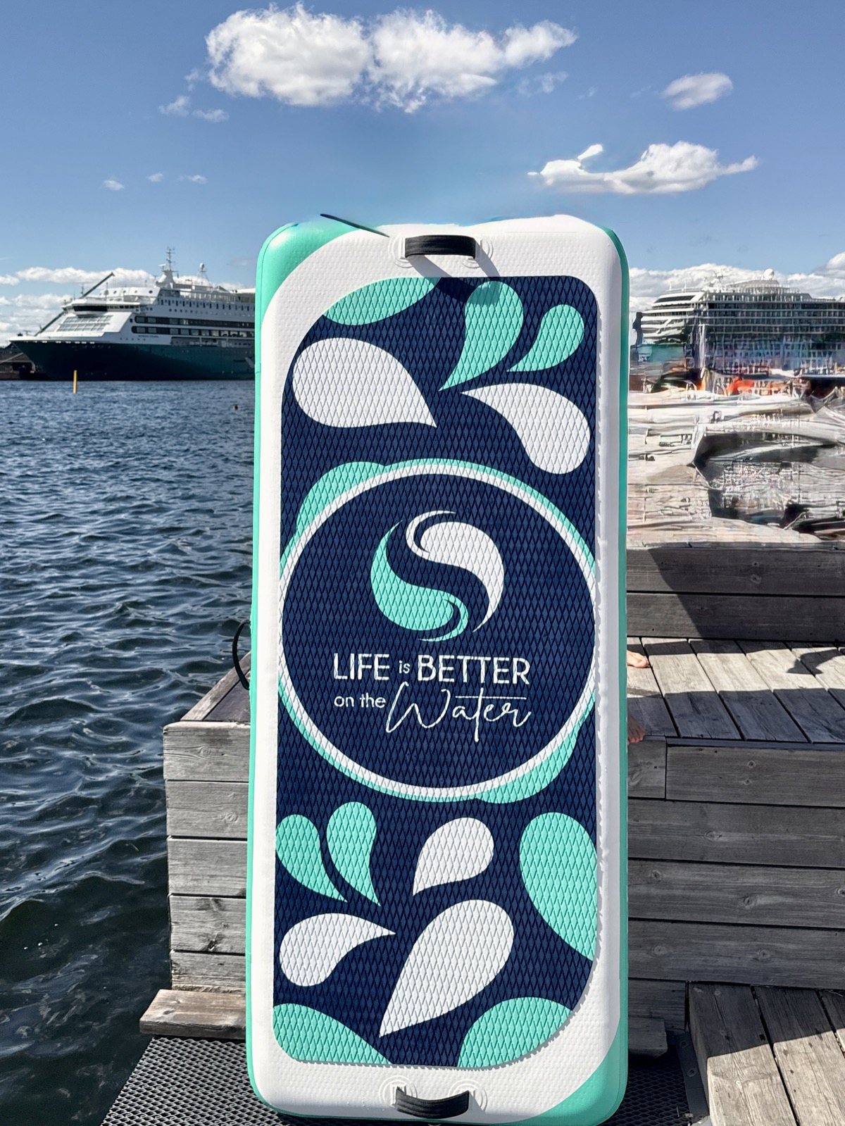 A custom-branded 'Life is Better on the Water' paddleboard standing on a dock by the water