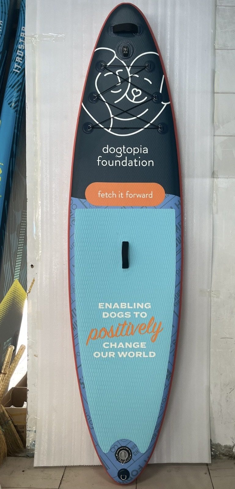 Paddleboard deck printed with a dog daycare logo, tagline and mission line