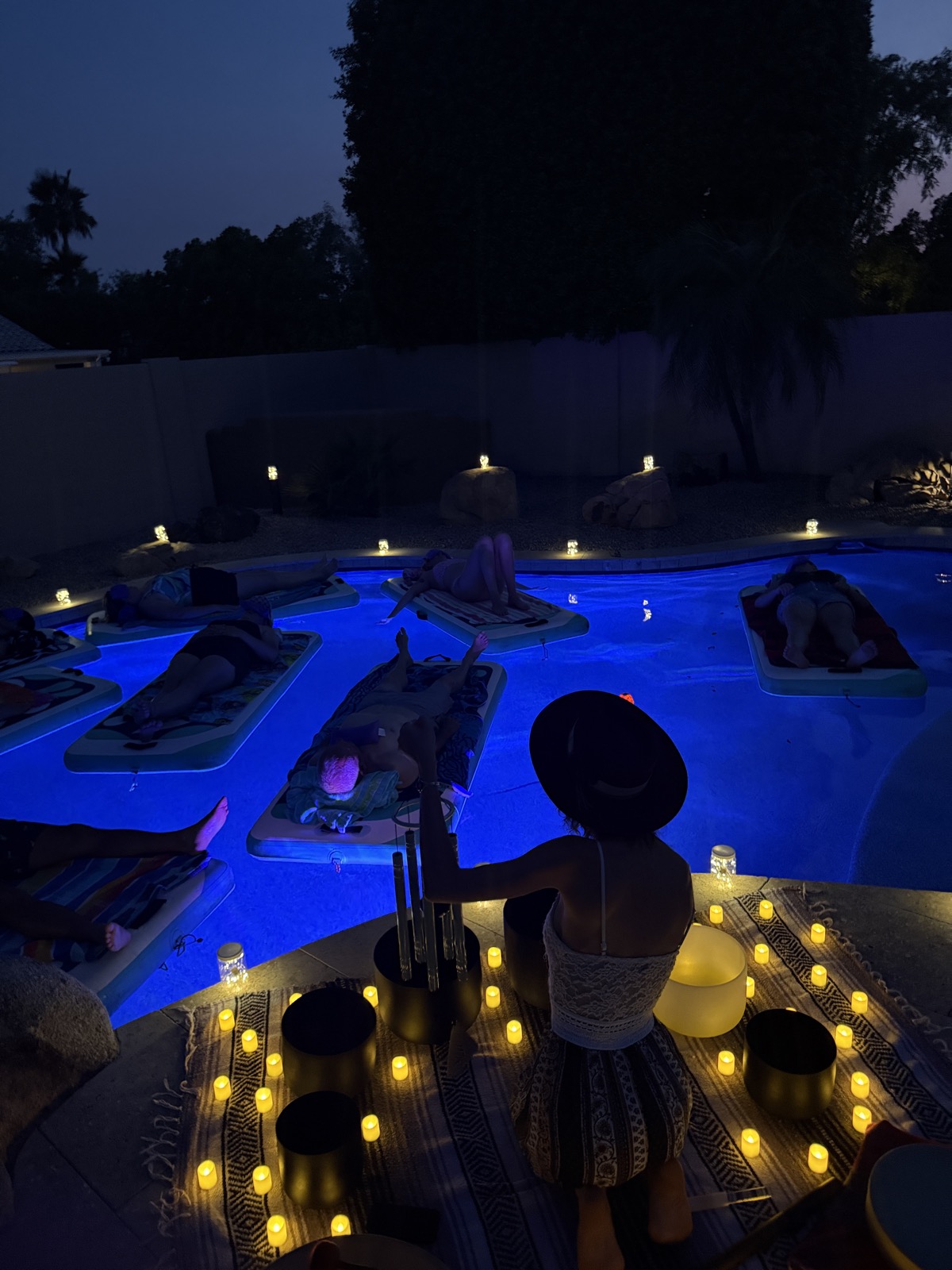 A twilight candlelit floating soundbath in a backyard pool
